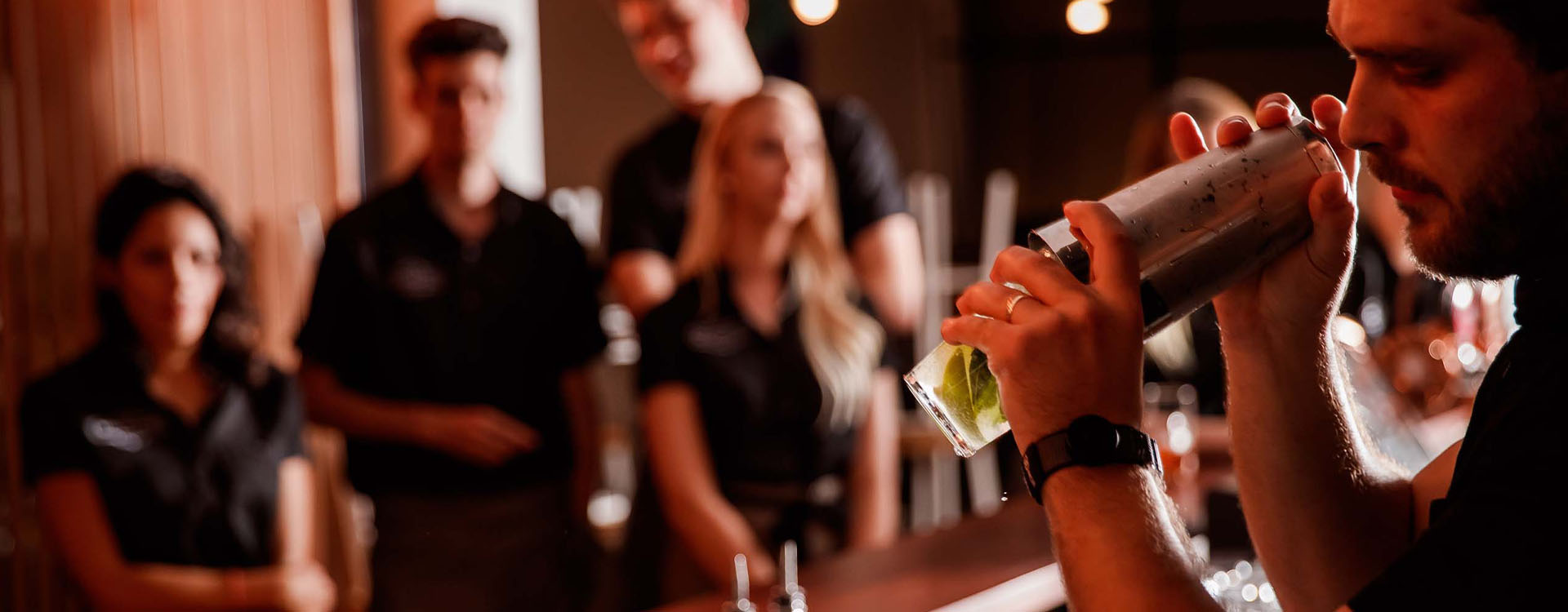 Bar tender teaching colleagues how to make cocktails behind bar.